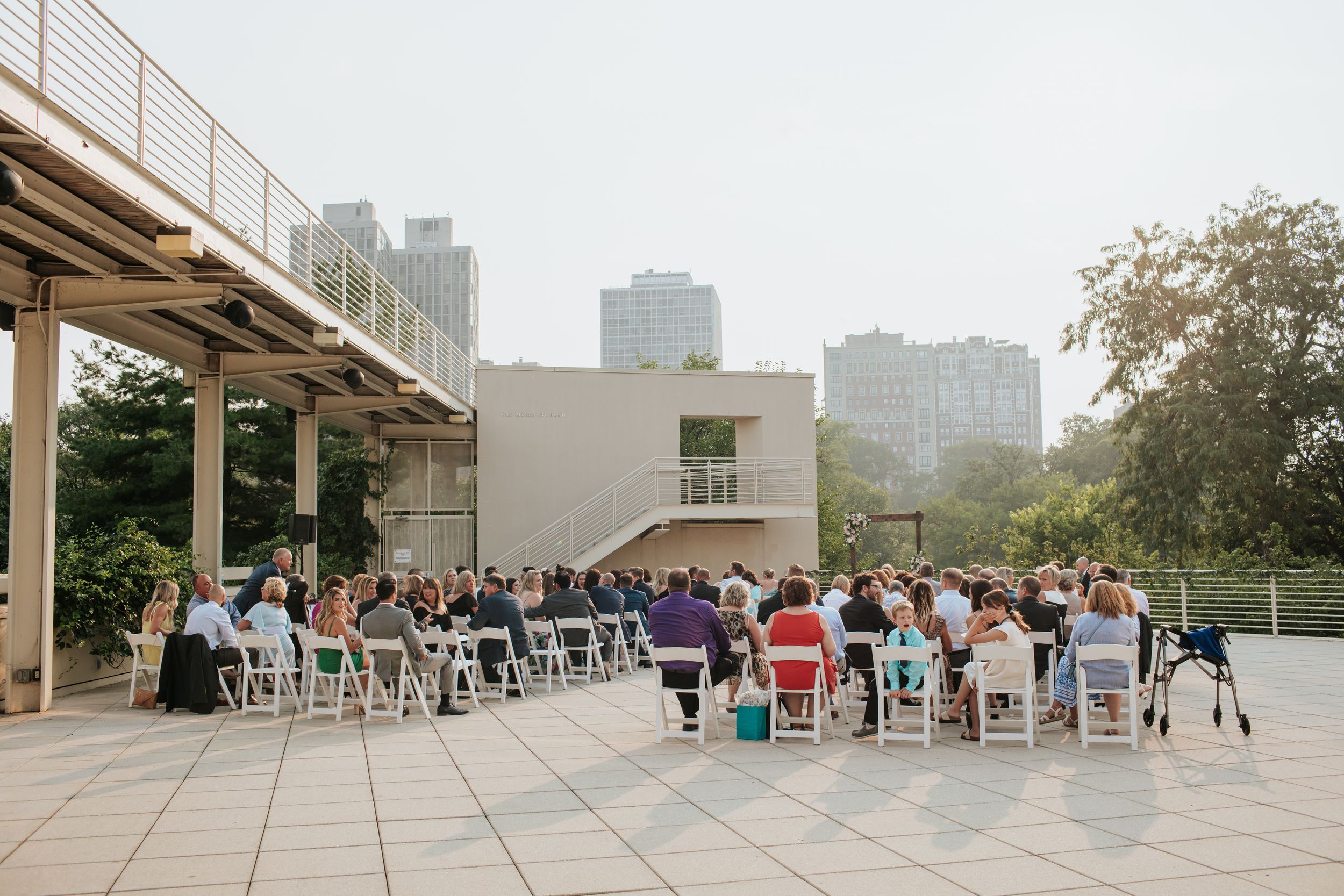 A panoramic view of people sitting in chairs on an outdoor terrace overlooking a city skyline.