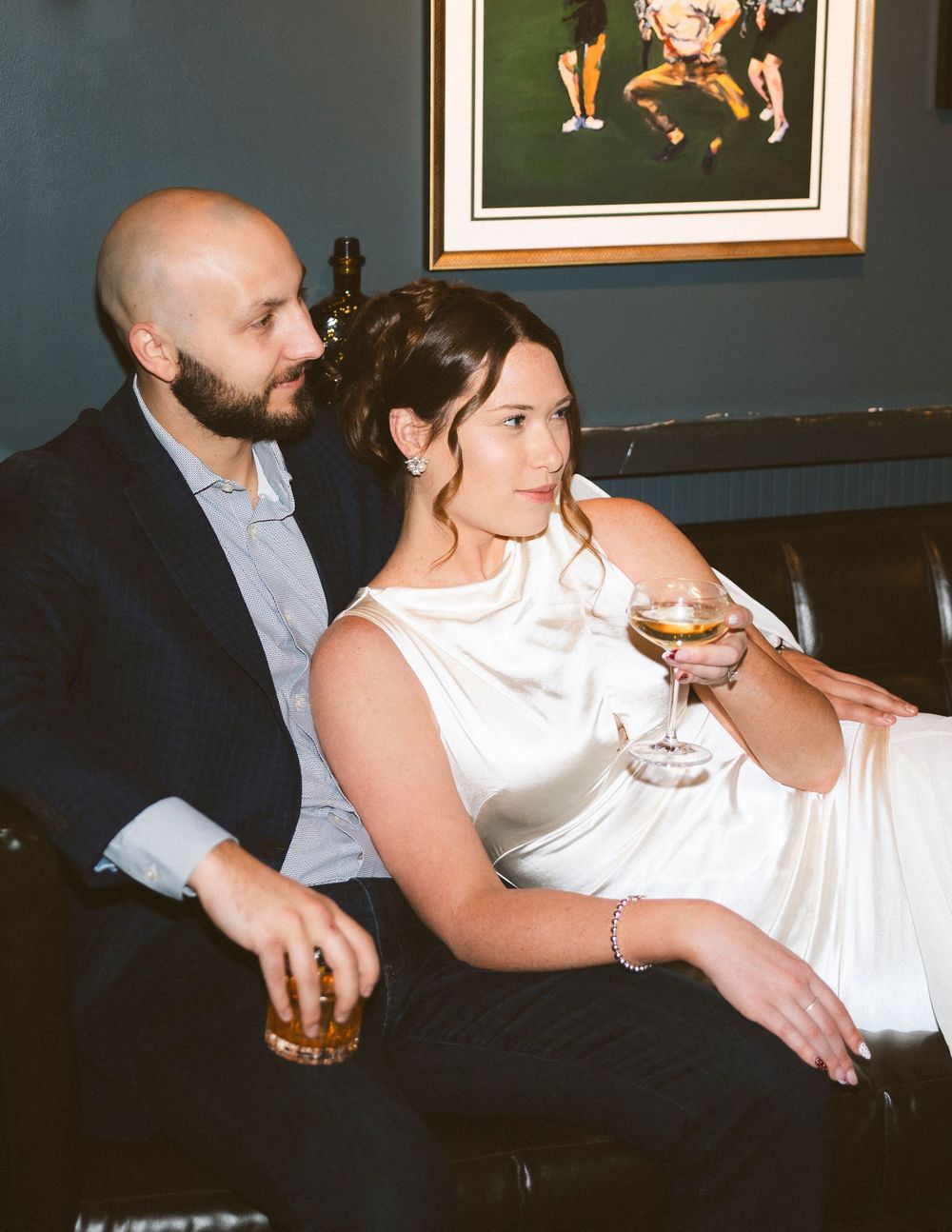 Couple relaxing together on a leather couch in a dimly lit room with artwork on the walls.