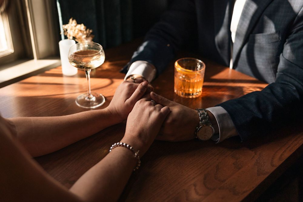 Drinks and hands visible on a wooden bar top illuminated by warm ambient lighting.