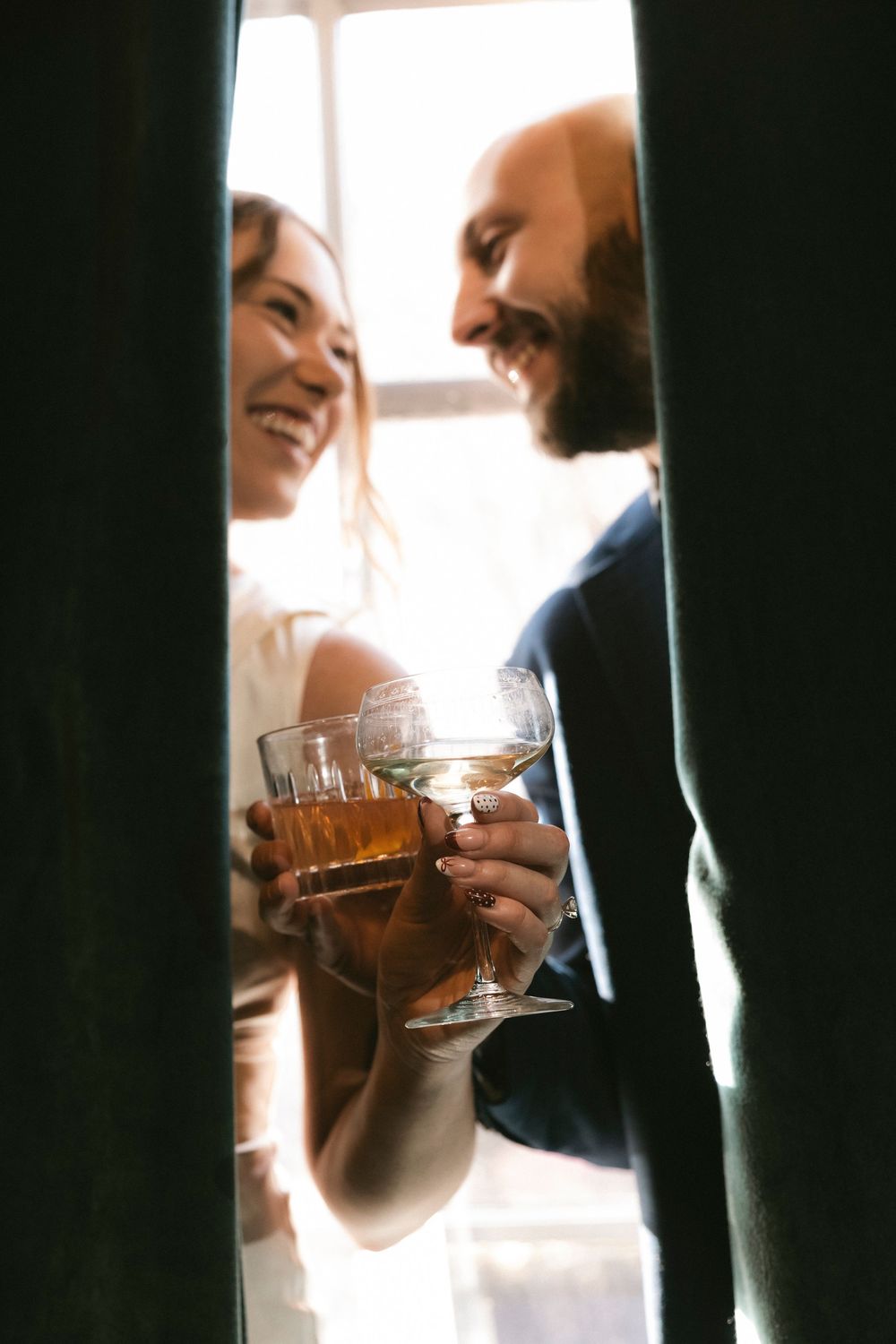 Two people sharing drinks and conversation in warm window light.