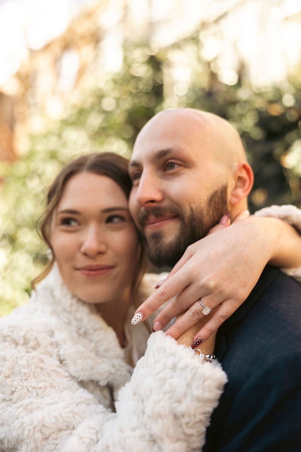 A couple embracing outdoors while showing off an engagement ring.
