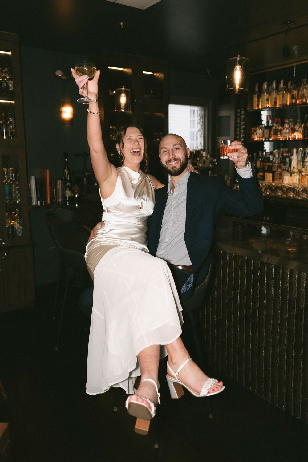 Joyful celebration at a bar with white dress and navy suit visible in dim lighting.