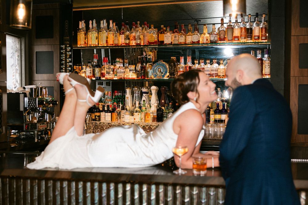 Bar scene with bottles illuminated on shelves and pendant lights creating warm ambiance.