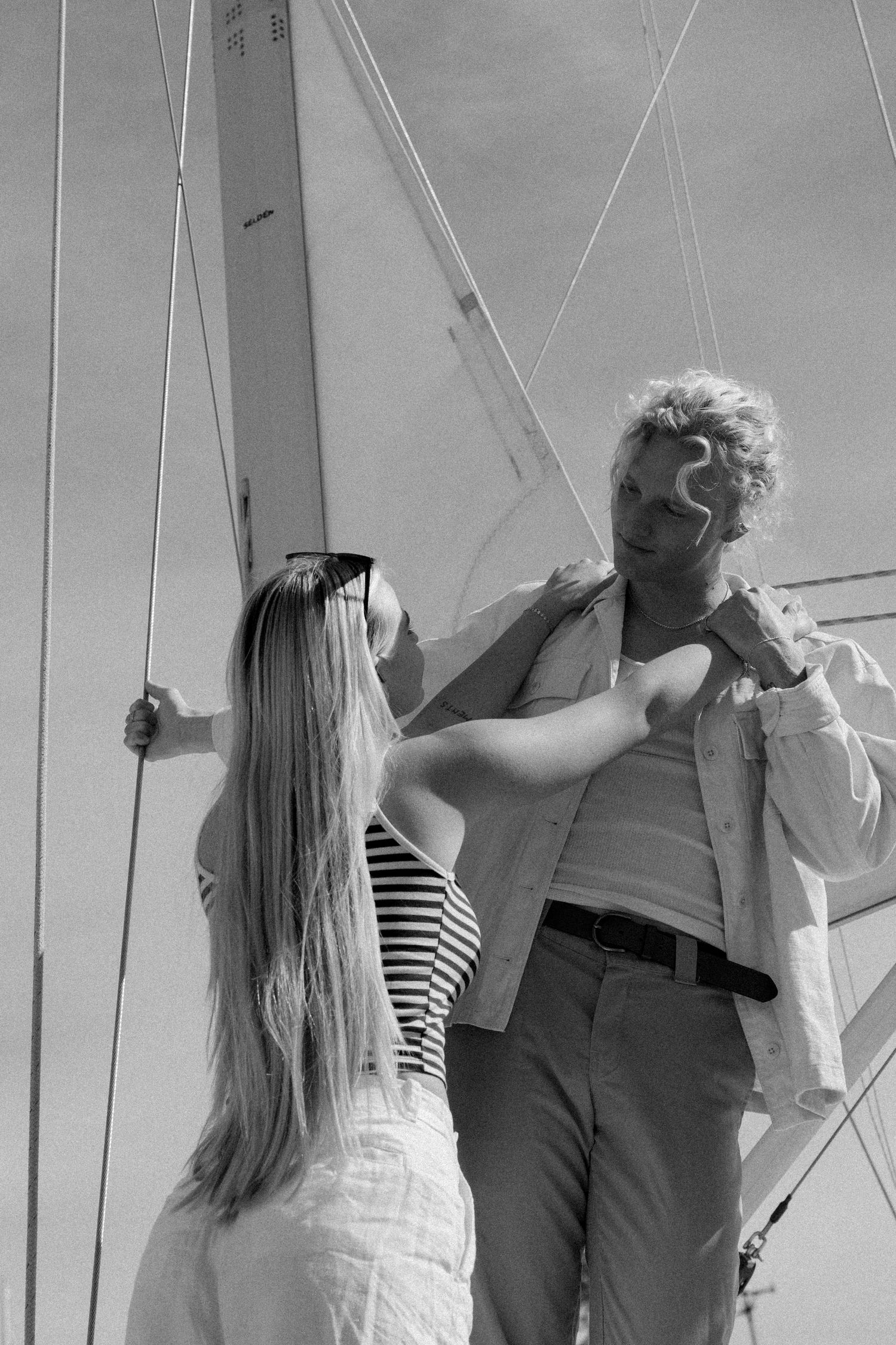 Black and white image of a couple on a sailboat against a bright sky.