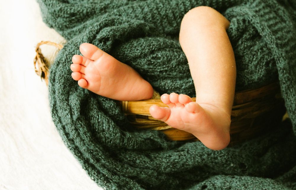 Tiny baby feet wrapped in a cozy green knitted blanket.