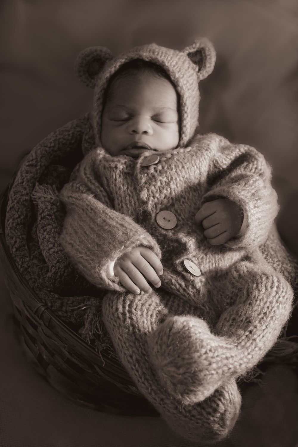 Sleeping newborn in knitted bear outfit placed in cozy basket.