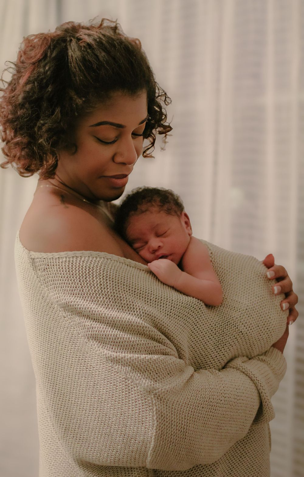 Mother in sweater holding sleeping newborn baby in warm embrace.