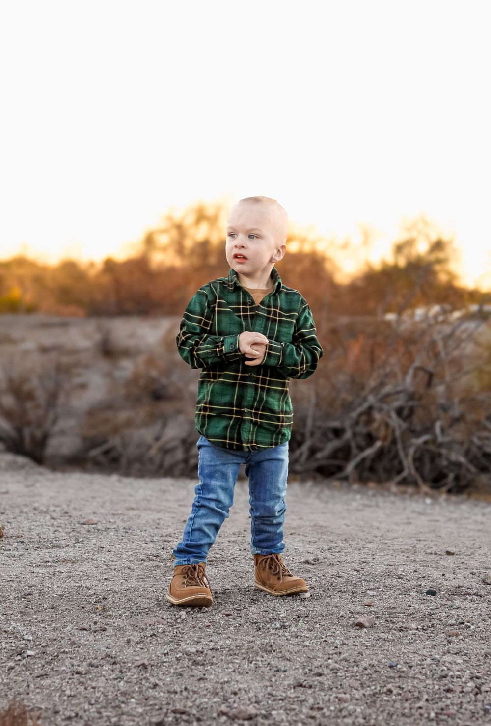 Child in green plaid shirt and jeans standing outdoors at golden hour.