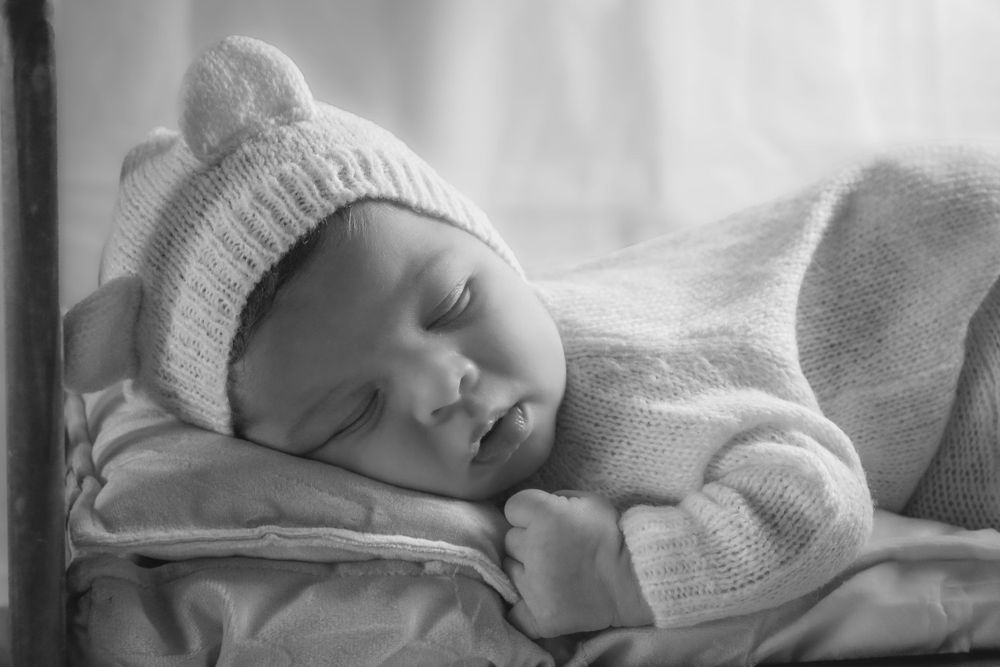 Peaceful sleeping baby wearing knit hat and sweater in black and white.