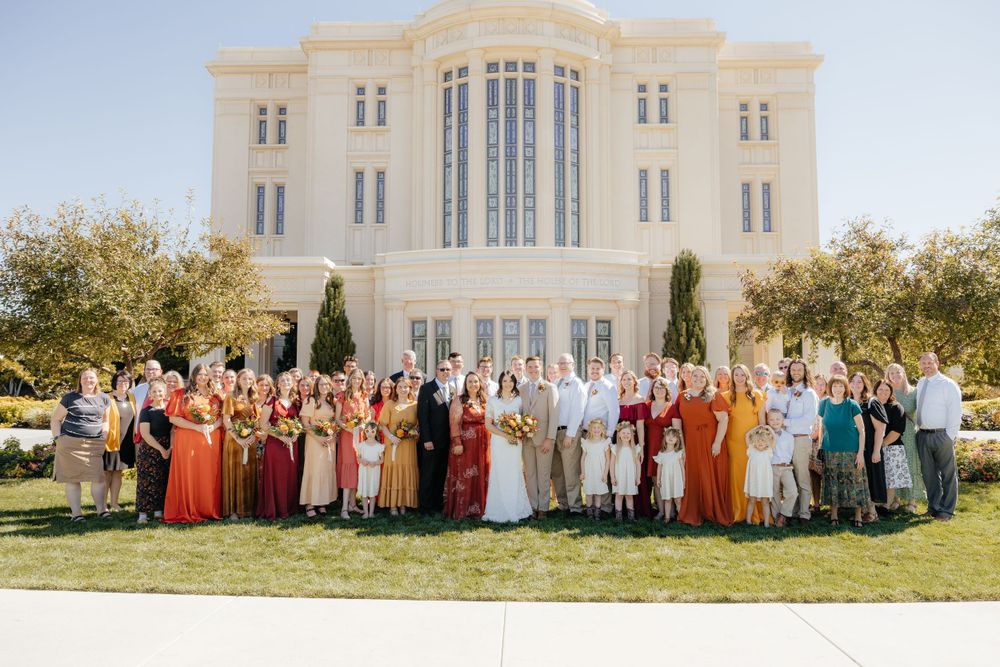Large wedding party poses in front of a grand LDS temple on a bright sunny autumn day.