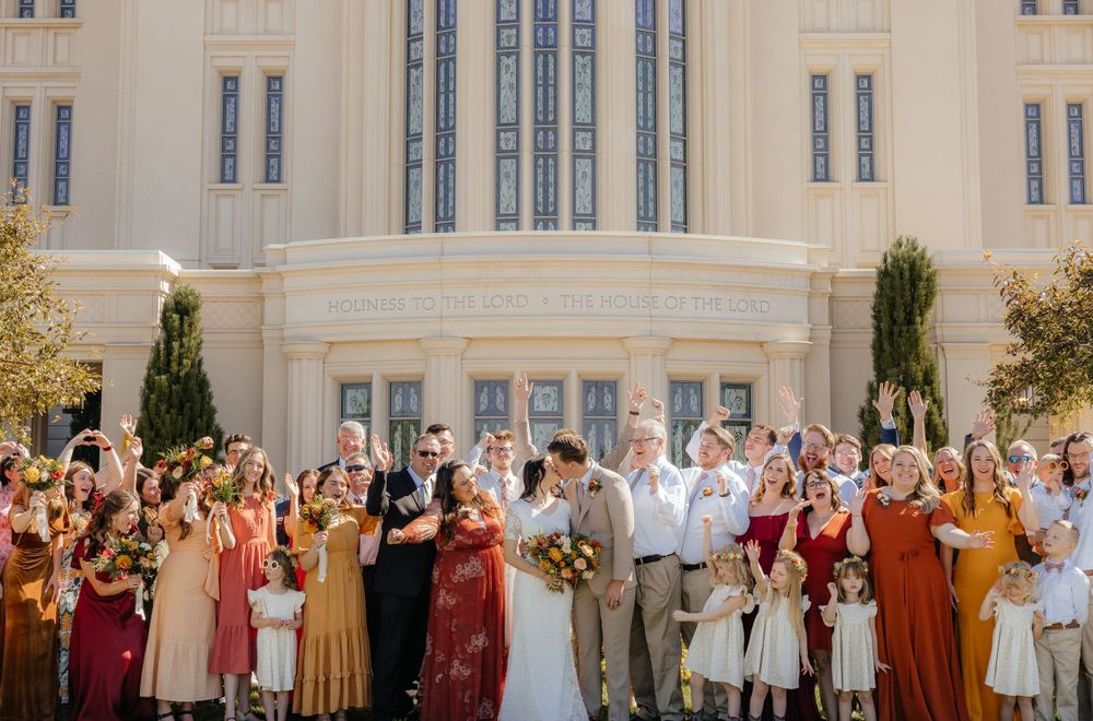 Excited wedding party cheers and celebrates in front of a beautiful LDS temple facade.
