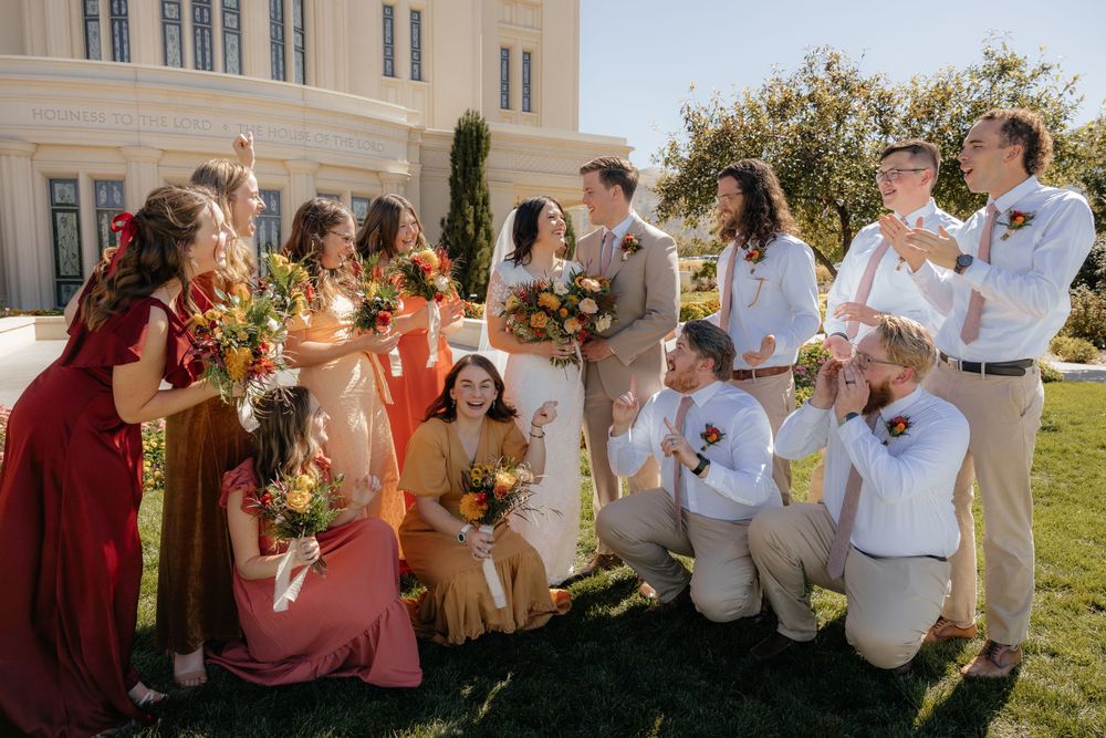 Wedding party laughing and celebrating together on the lawn outside a beautiful white temple.