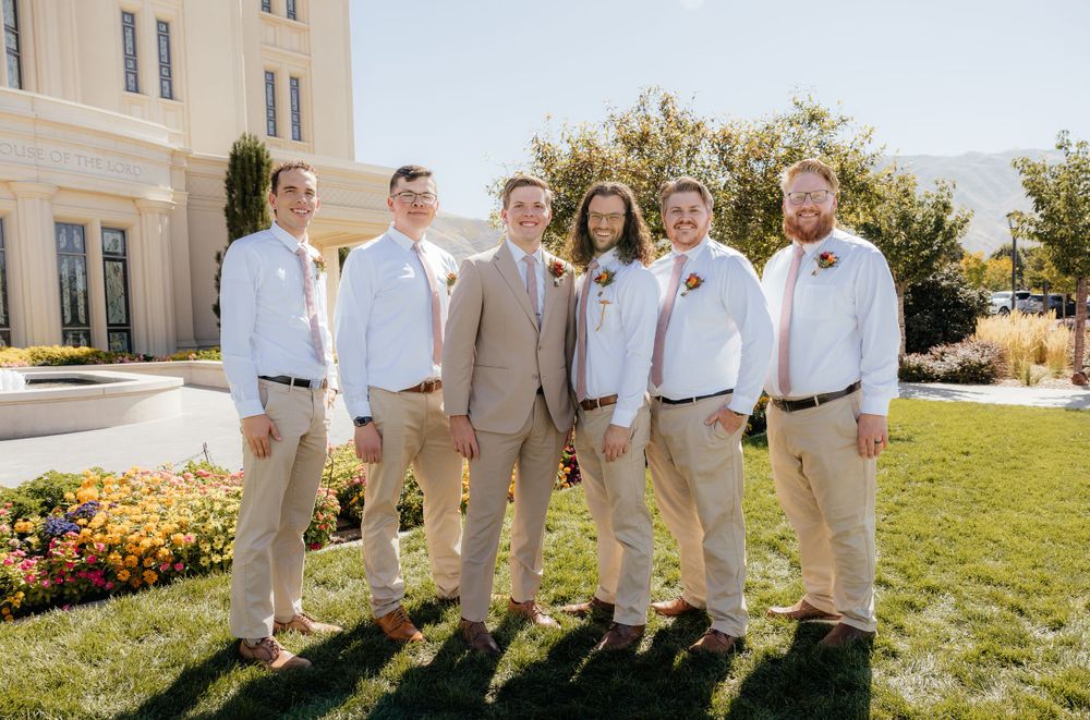 Groom and groomsmen in tan pants and white shirts posing together outside a temple.