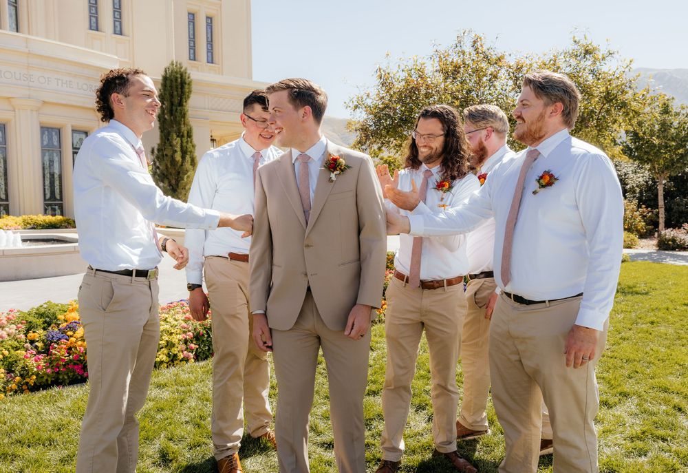 Groomsmen congratulating the groom in tan suit outside a temple on a sunny day.