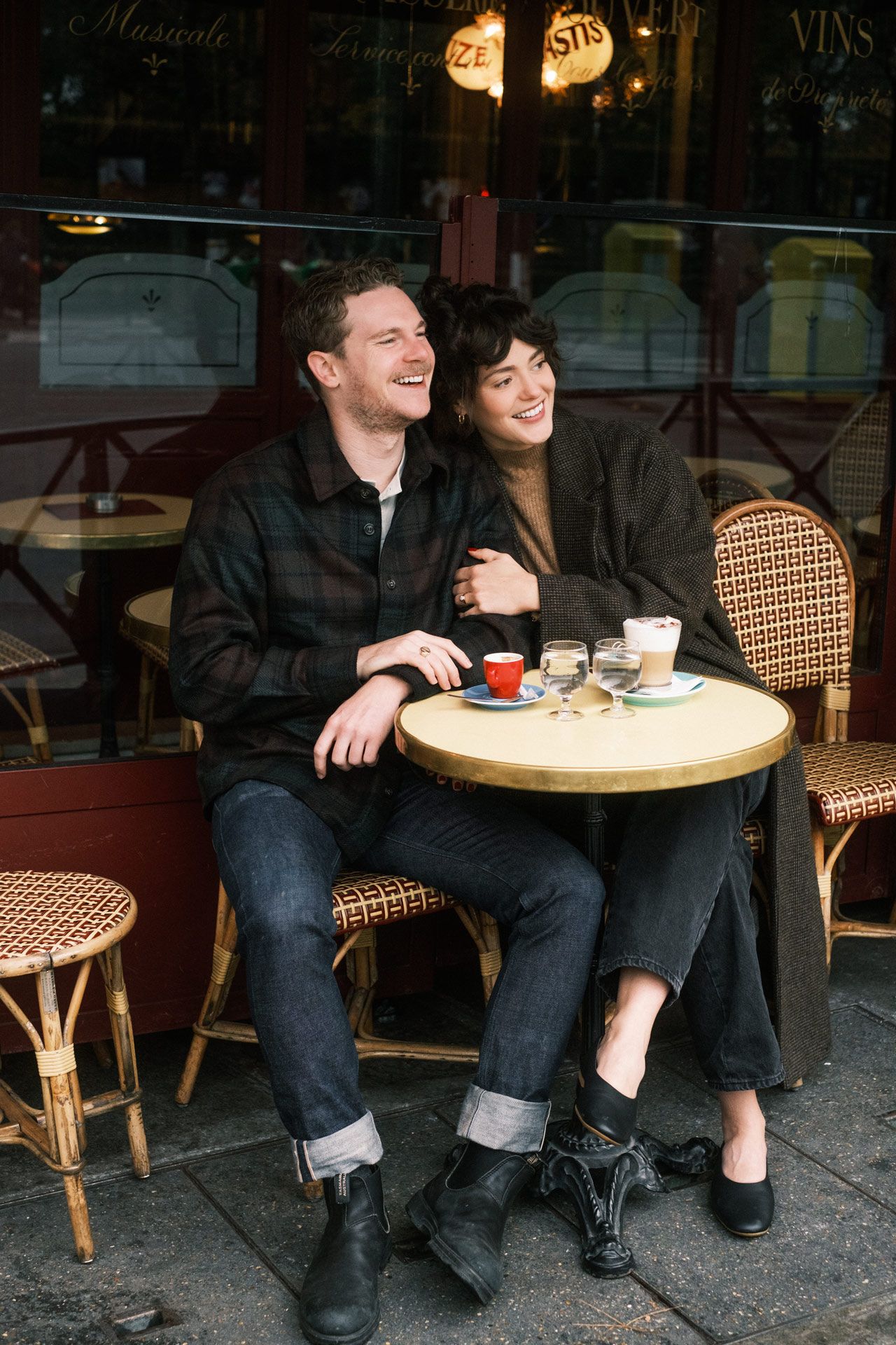 Couple enjoying coffee and conversation at a charming Parisian sidewalk cafe with rattan chairs and round table.