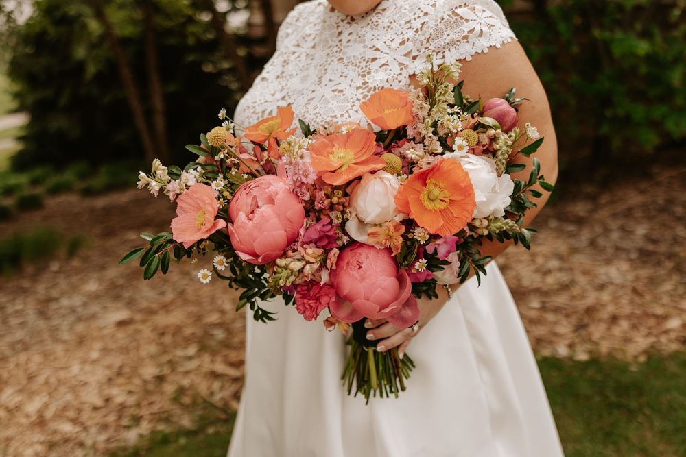 A romantic garden wedding ceremony scene with coral and blush pink floral bouquets and natural outdoor decor.