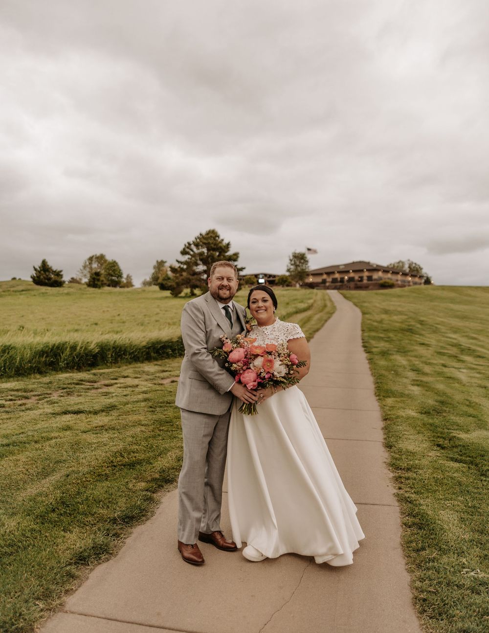 Couple walking and posing along a winding concrete path through grassy hills on an overcast day.