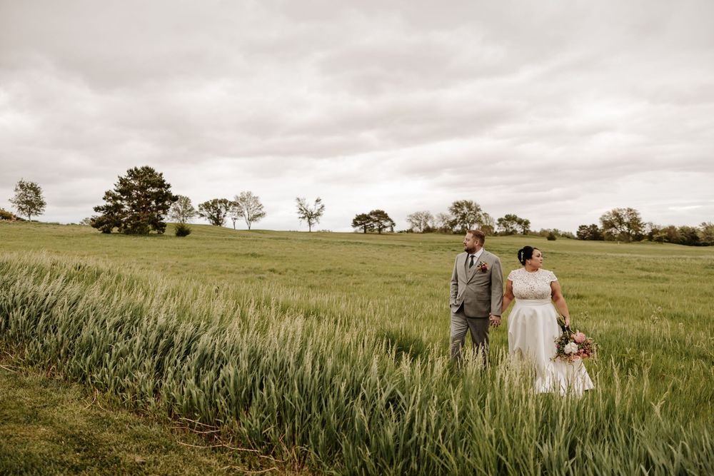 A couple walks through a lush green wheat field on an overcast day in the countryside.