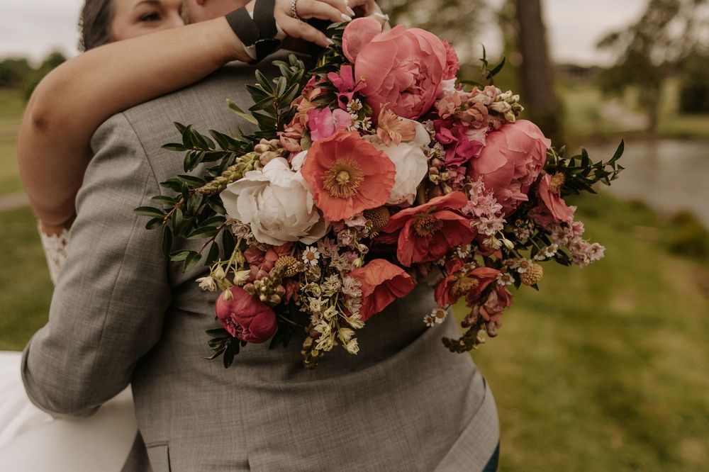 A collection of wedding detail photos showing pink and coral floral bouquets held against a grey suit background.