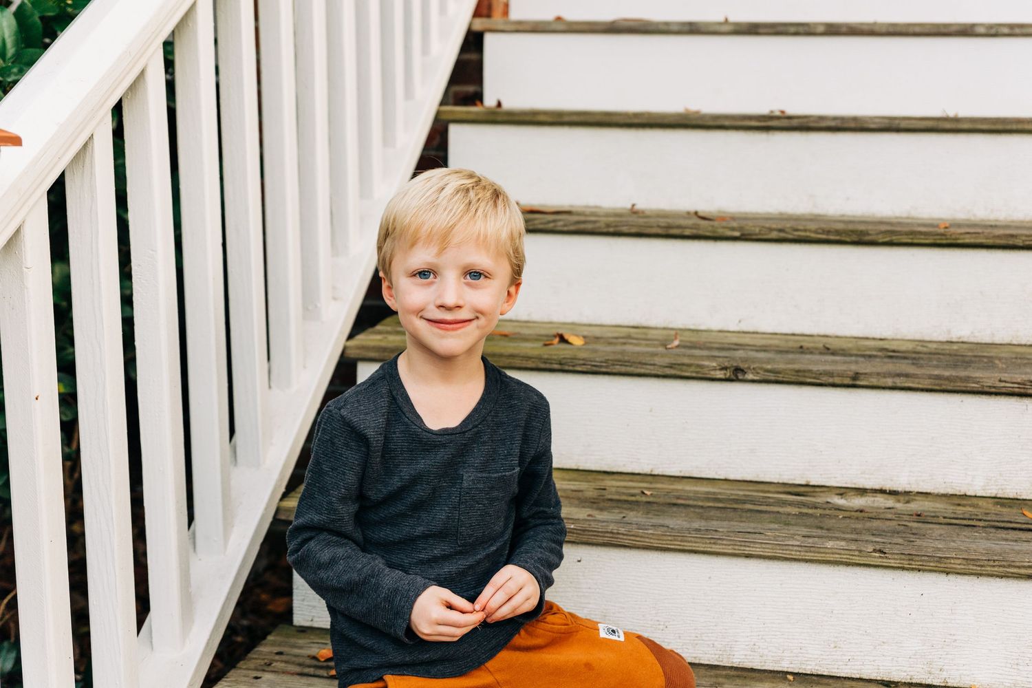 A young child in a navy sweater sits on wooden stairs with white railings.