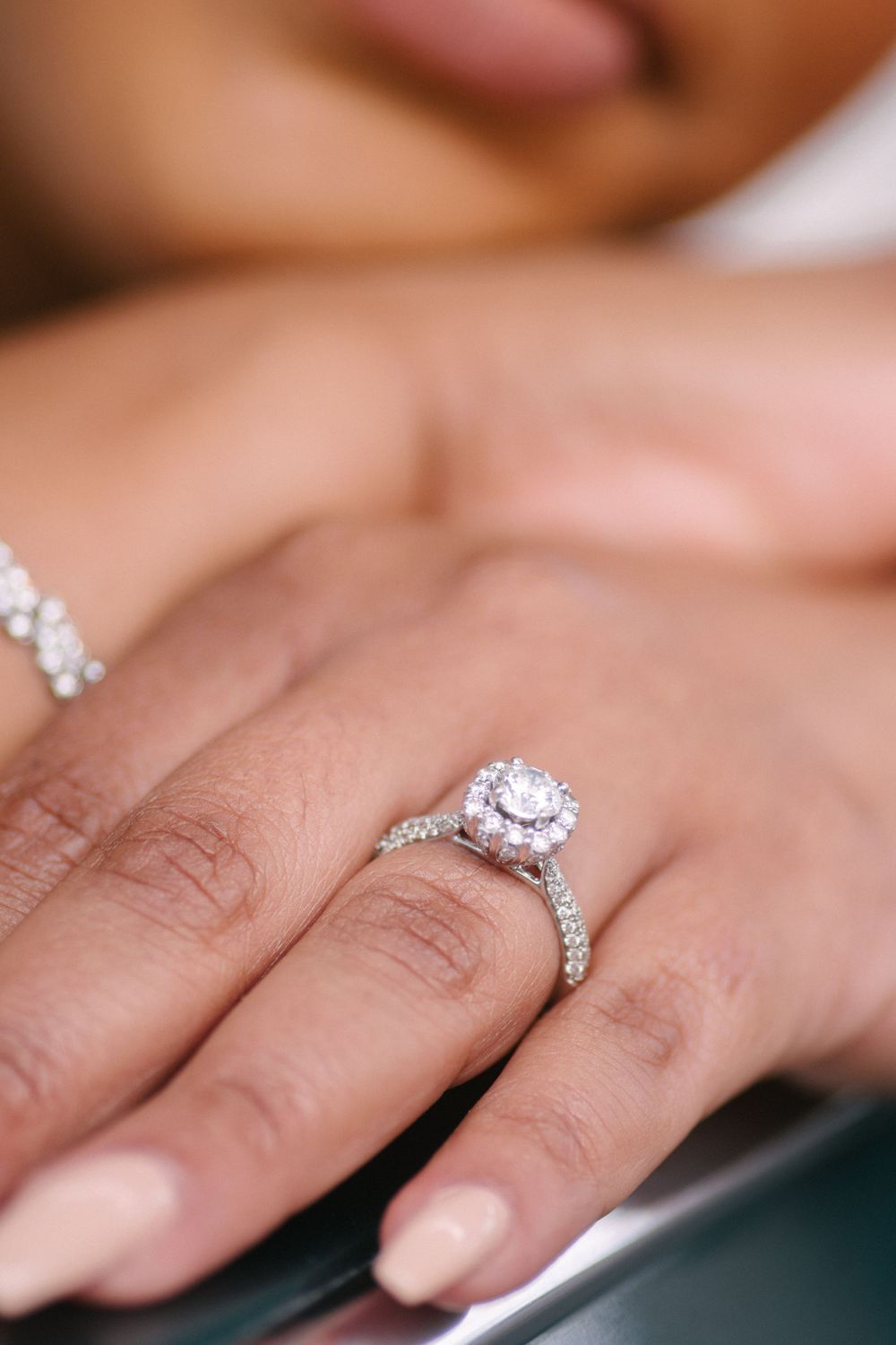 A delicate diamond engagement ring with a round center stone and pave band sparkles on a person's hand.