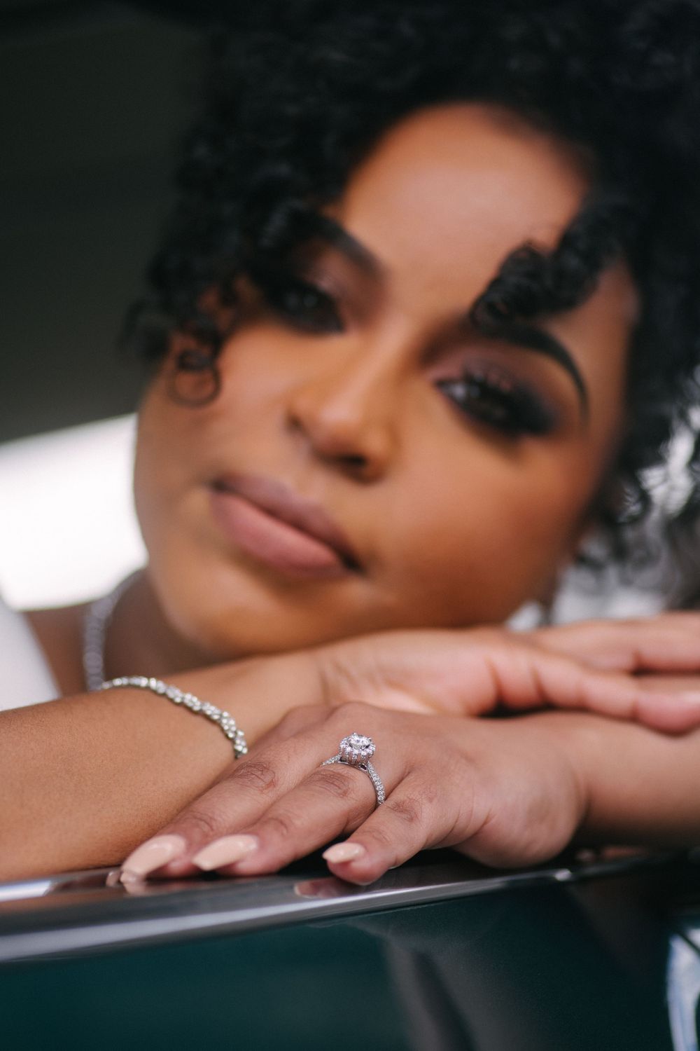 Sparkling engagement rings and wedding bands displayed on hands laying against a dark background.