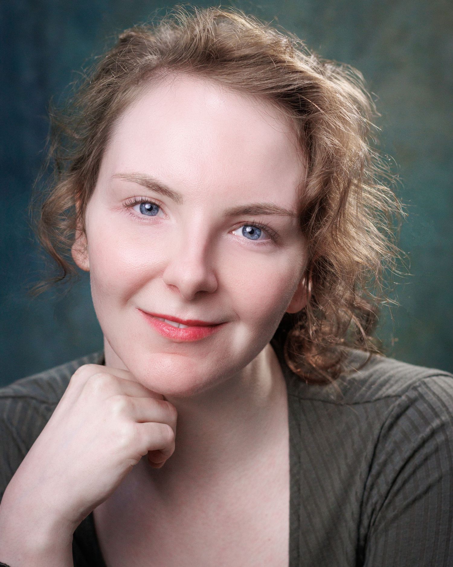 Professional portrait with curly hair and wearing a gray top against a muted background.
