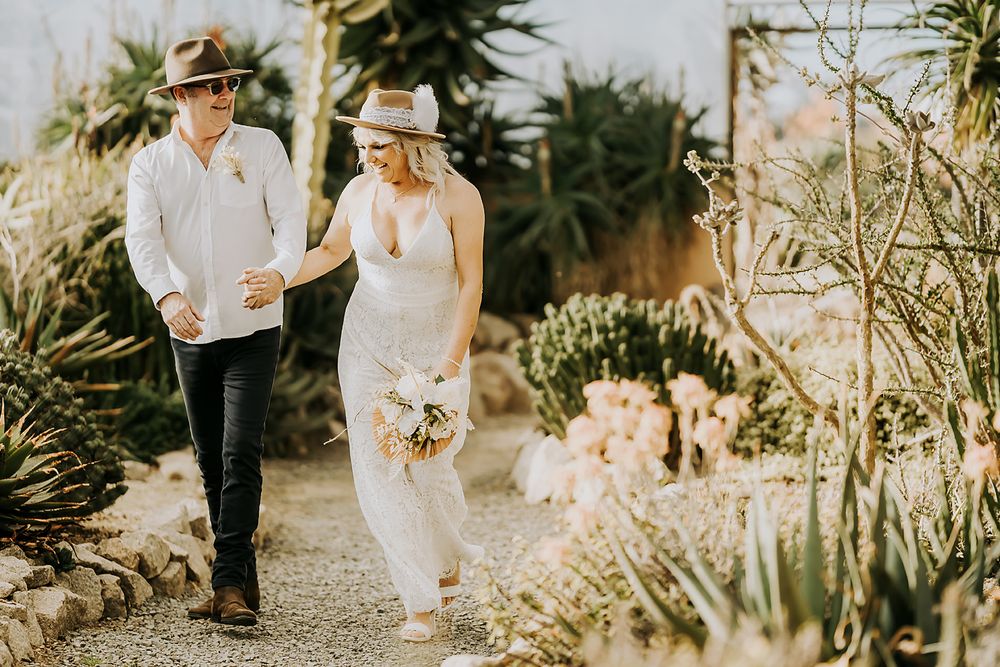 Outdoor wedding scene with guests walking along a winding desert garden path at sunset.