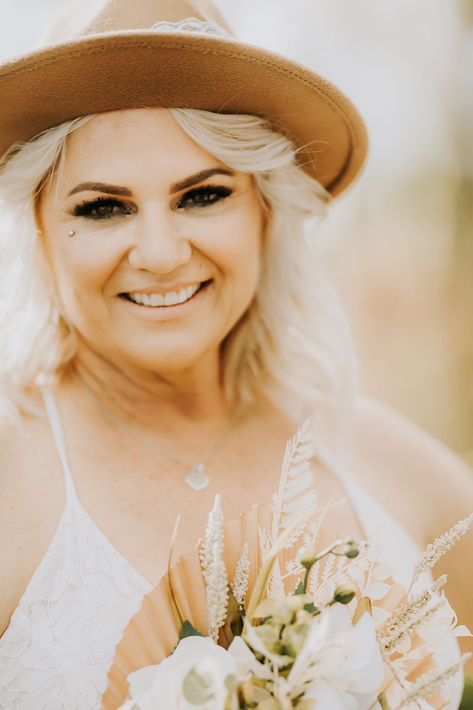 A person wearing a brown hat and white dress holds a delicate bouquet of white flowers on their wedding day.