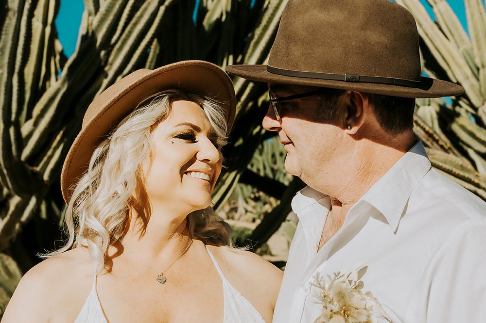 Couple in western hats sharing a tender moment against bamboo backdrop.
