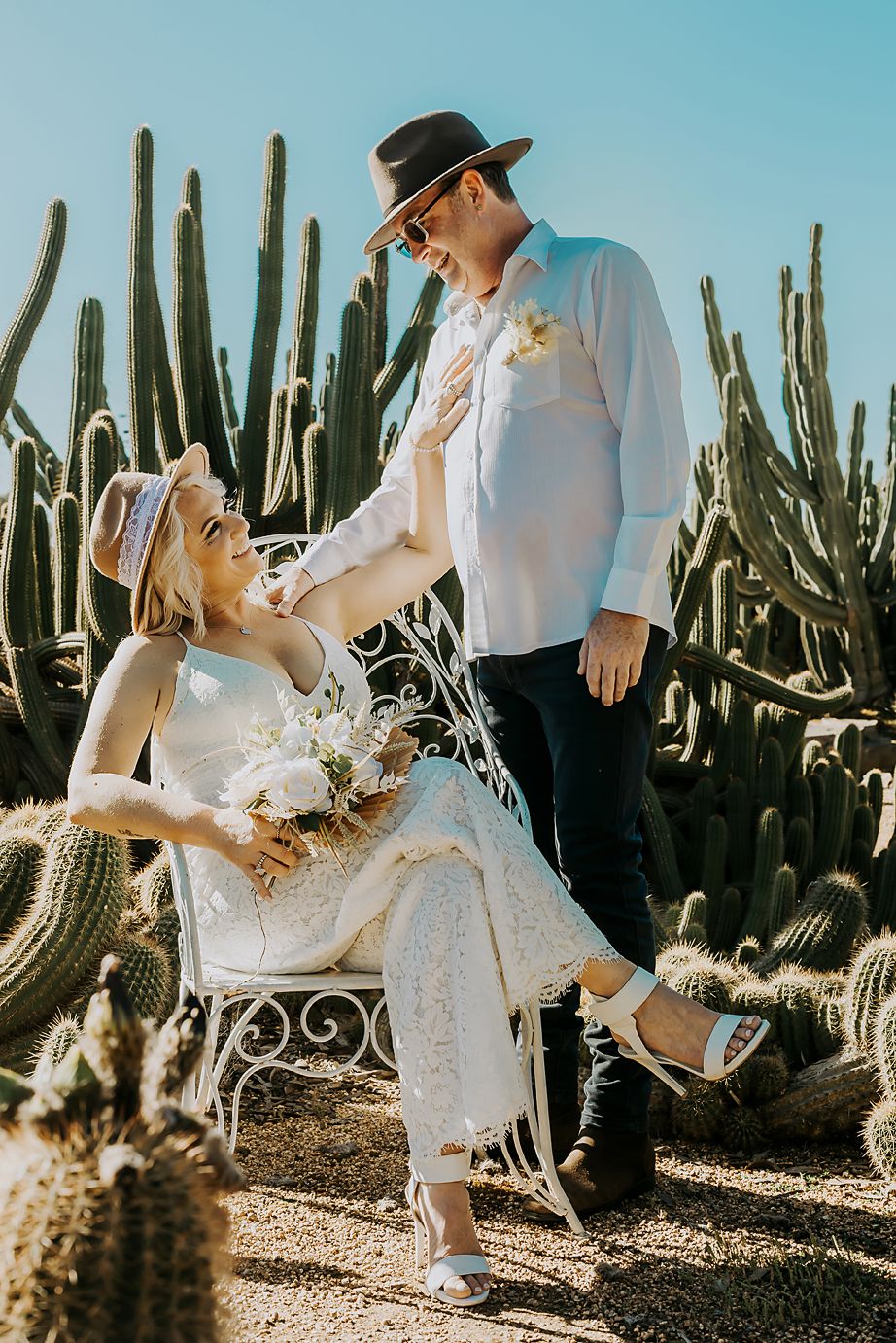 A couple shares a romantic moment in a desert garden surrounded by tall cactus plants on their wedding day.