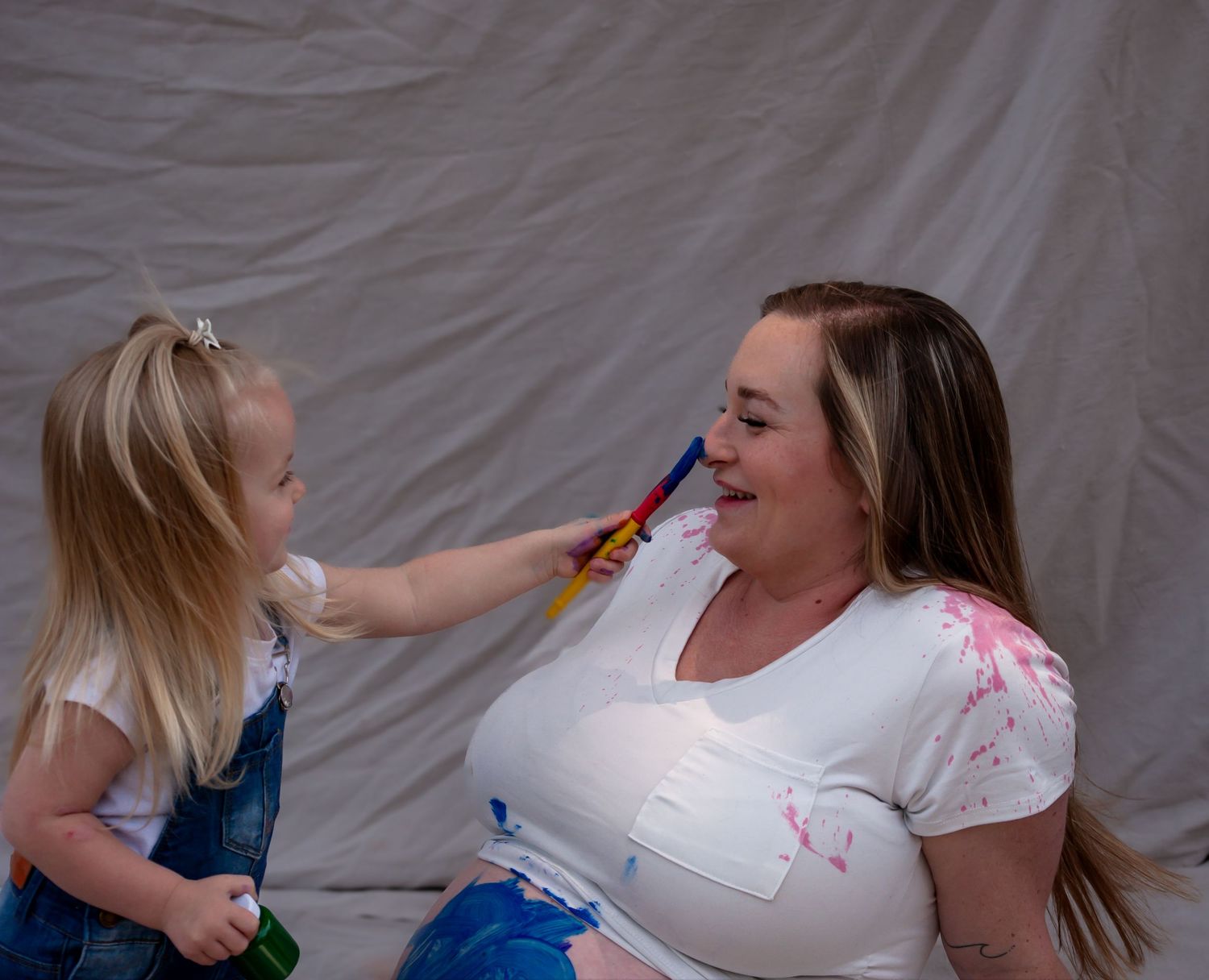 A small child putting paint on her mothers nose.