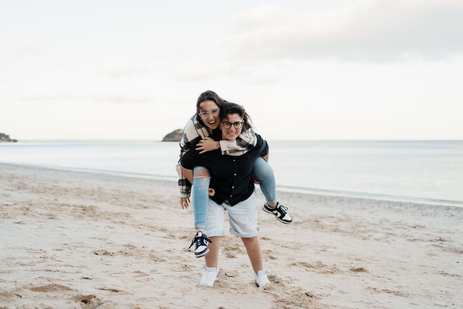 A playful moment captured between two companions running along a sandy beach at the water's edge.