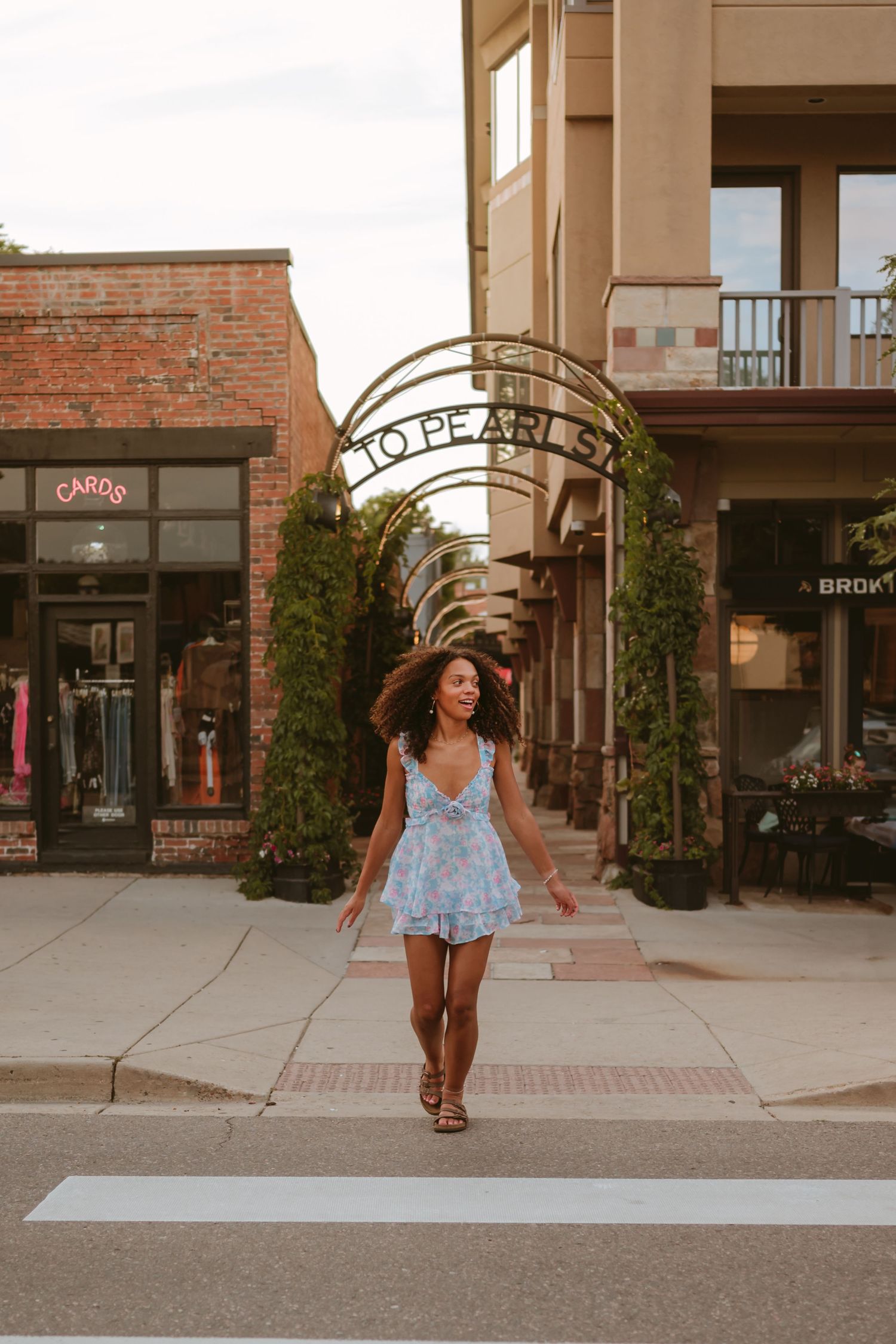 Woman in a blue floral dress walks beneath decorative archways at an outdoor shopping plaza.