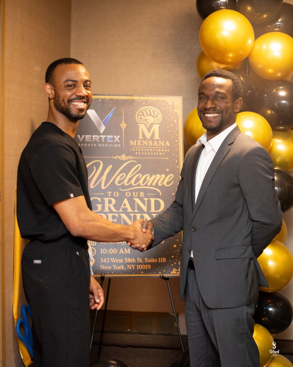 Two men shaking hands at a Vertex and Mensana grand opening event with gold and black balloon decorations.