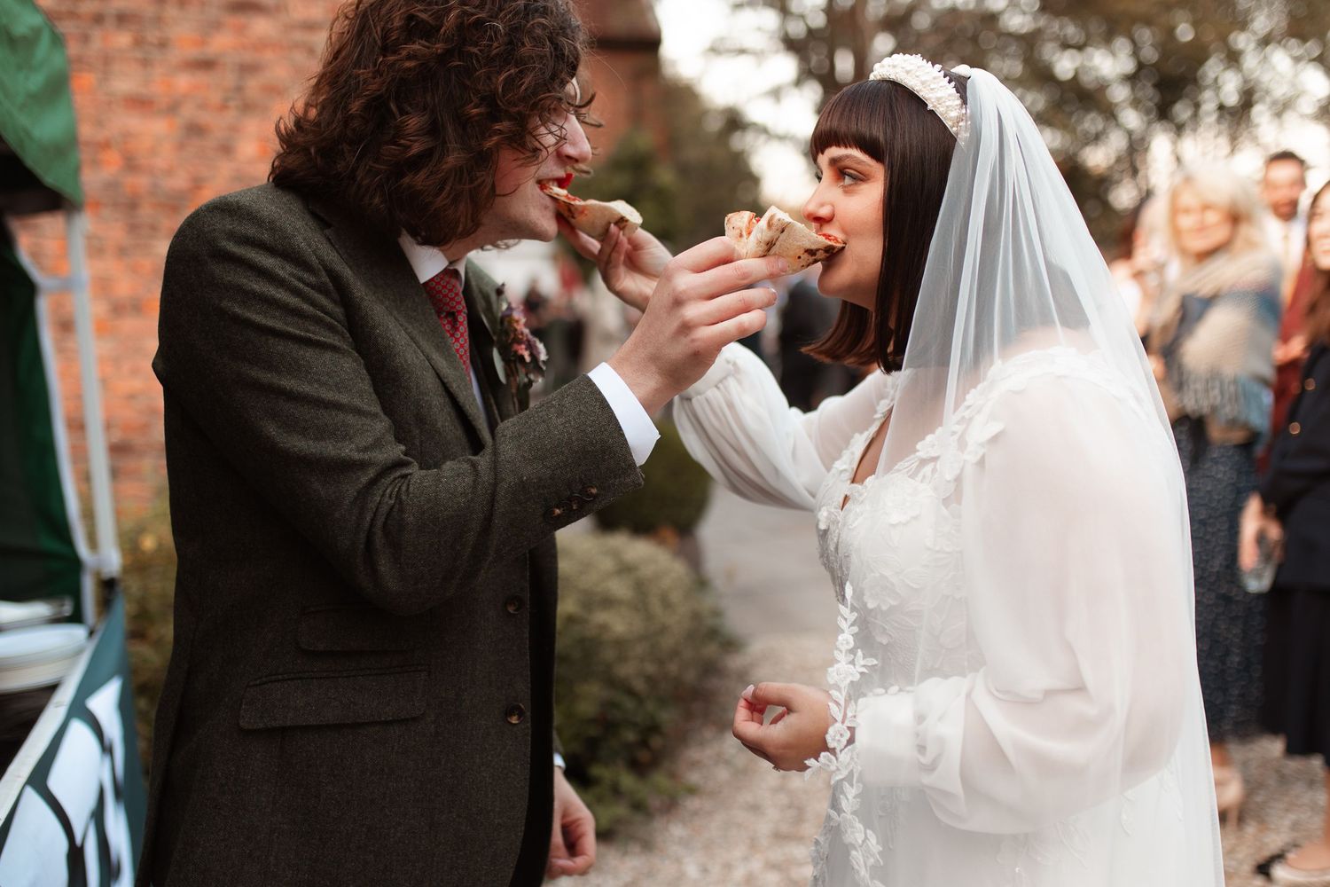 A wedding couple stands in a stone archway while guests gather around during an outdoor ceremony.