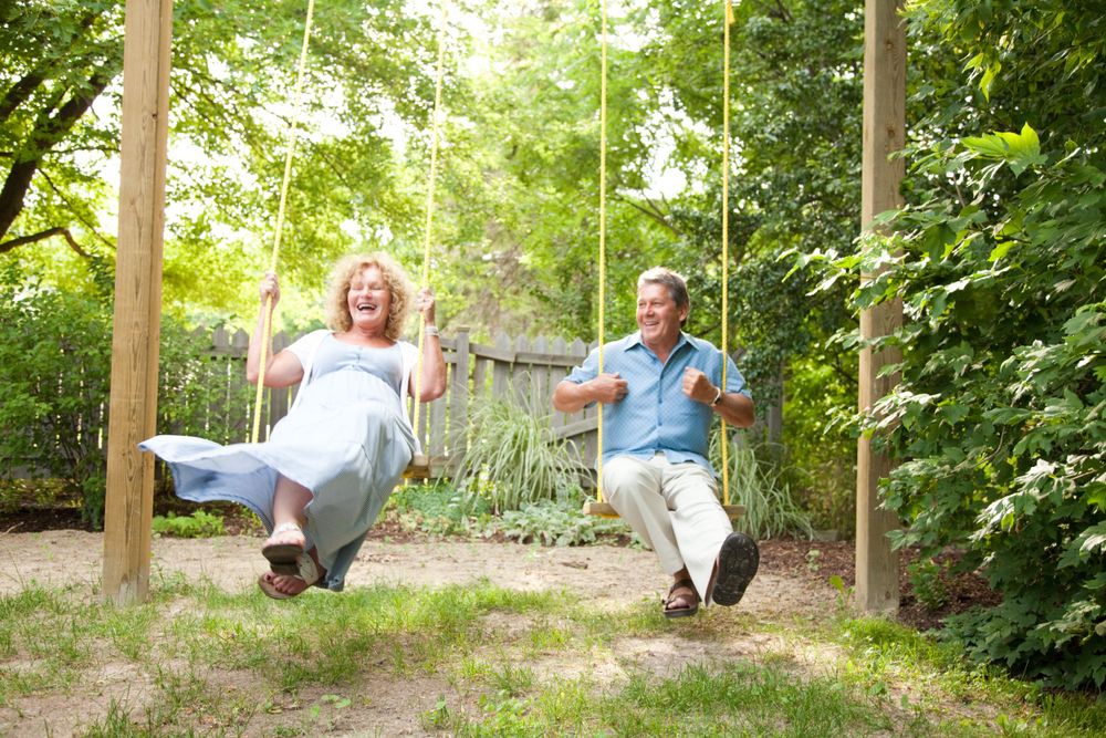 A mature couple enjoying themselves on wooden swings in a lush backyard garden.