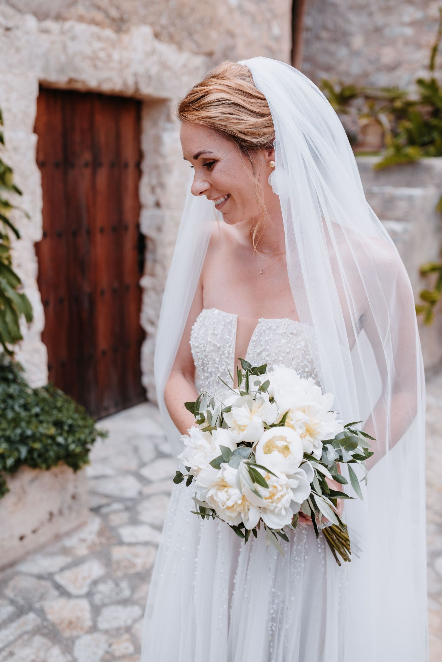 Elegante Brautporträtserie mit einem mit Perlen bestickten Brautkleid, einem fließenden Schleier und einem weißen Blumenstrauß.