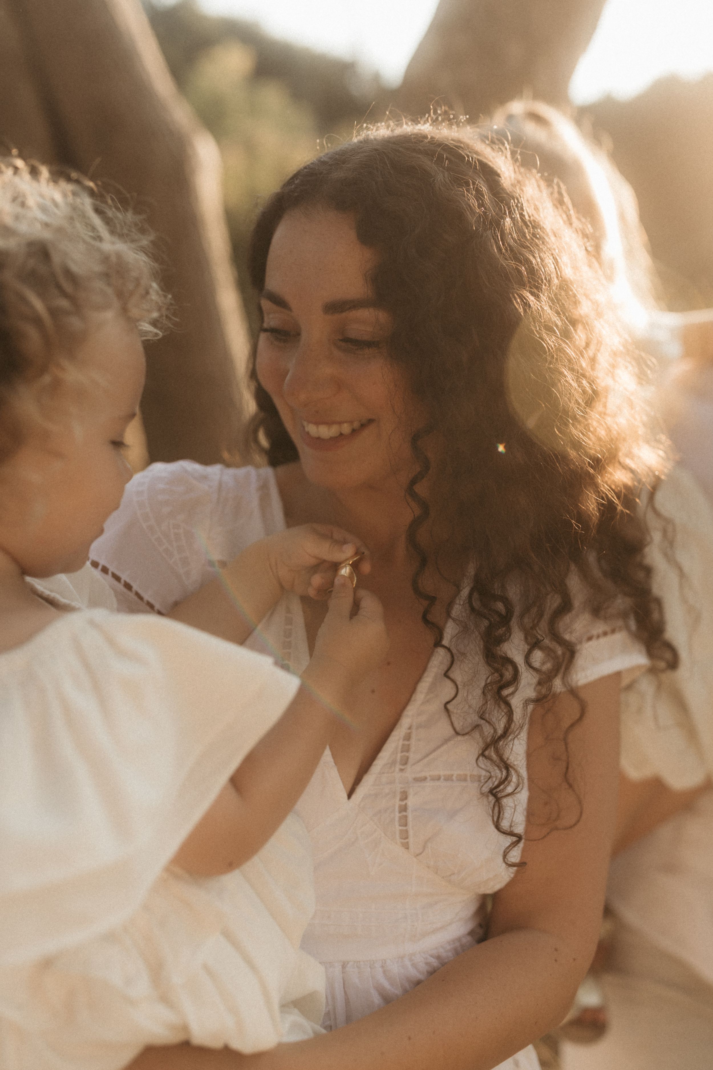 Parent and child share a tender moment together in soft sunlit white clothing.
