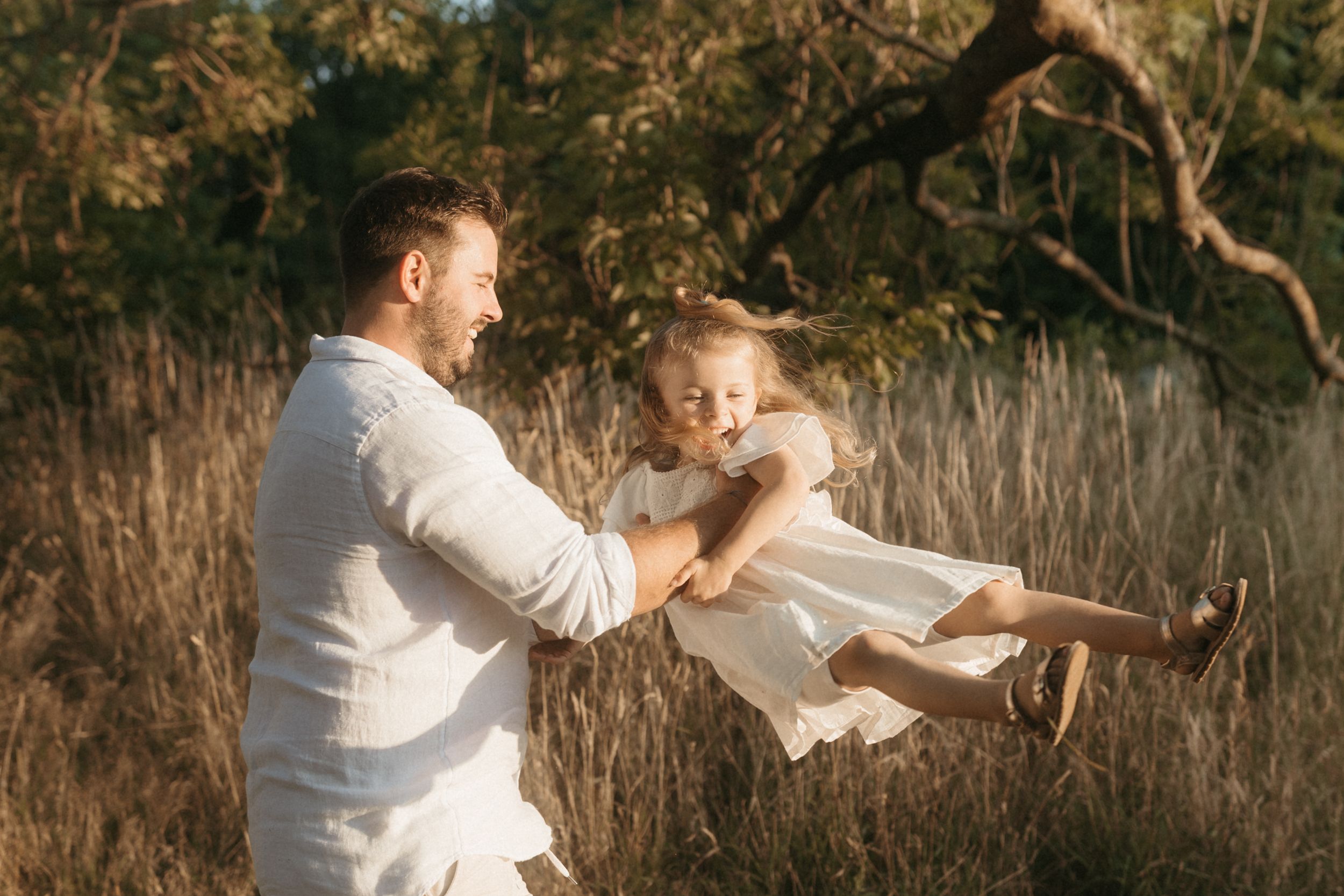 A tender moment captured in golden light as two people play together in a field with tall grass.