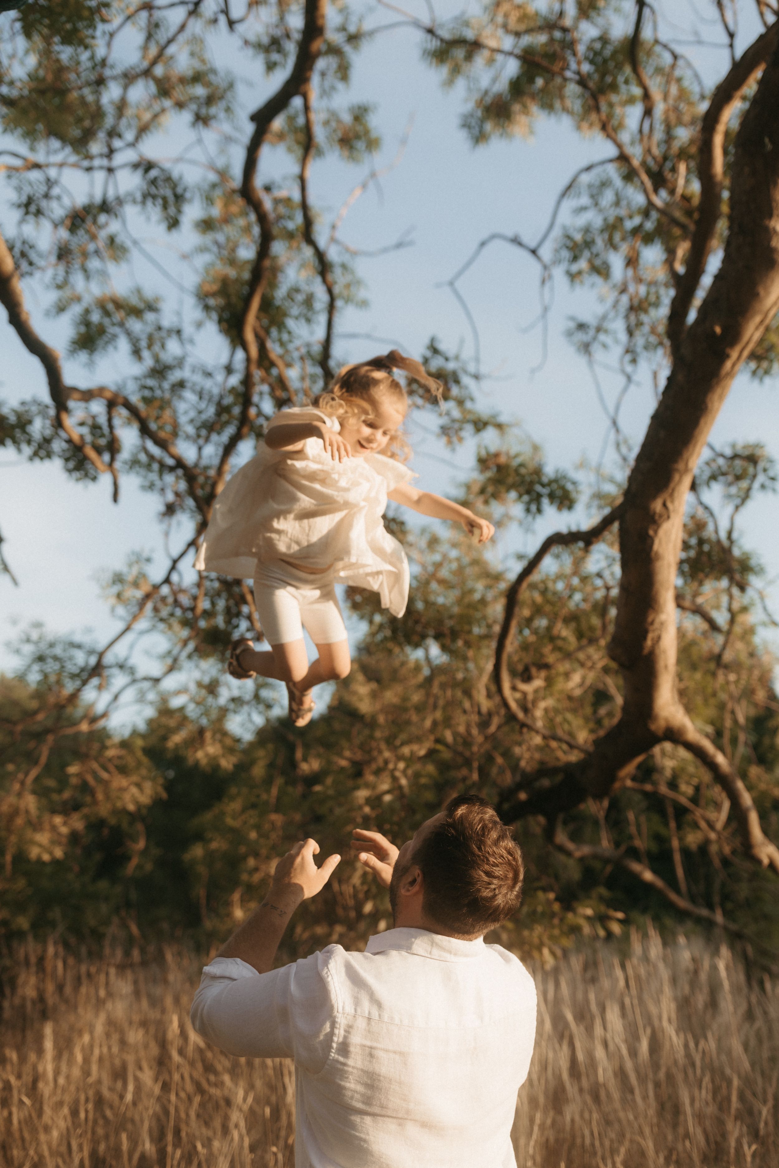 A parent throwing a child up in the air in a playful sequence against a sunset backlit natural setting.