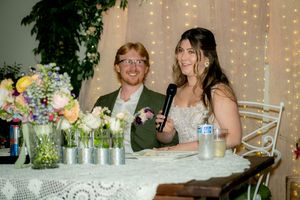 A couple sits at their wedding reception table decorated with spring flowers and fairy lights.