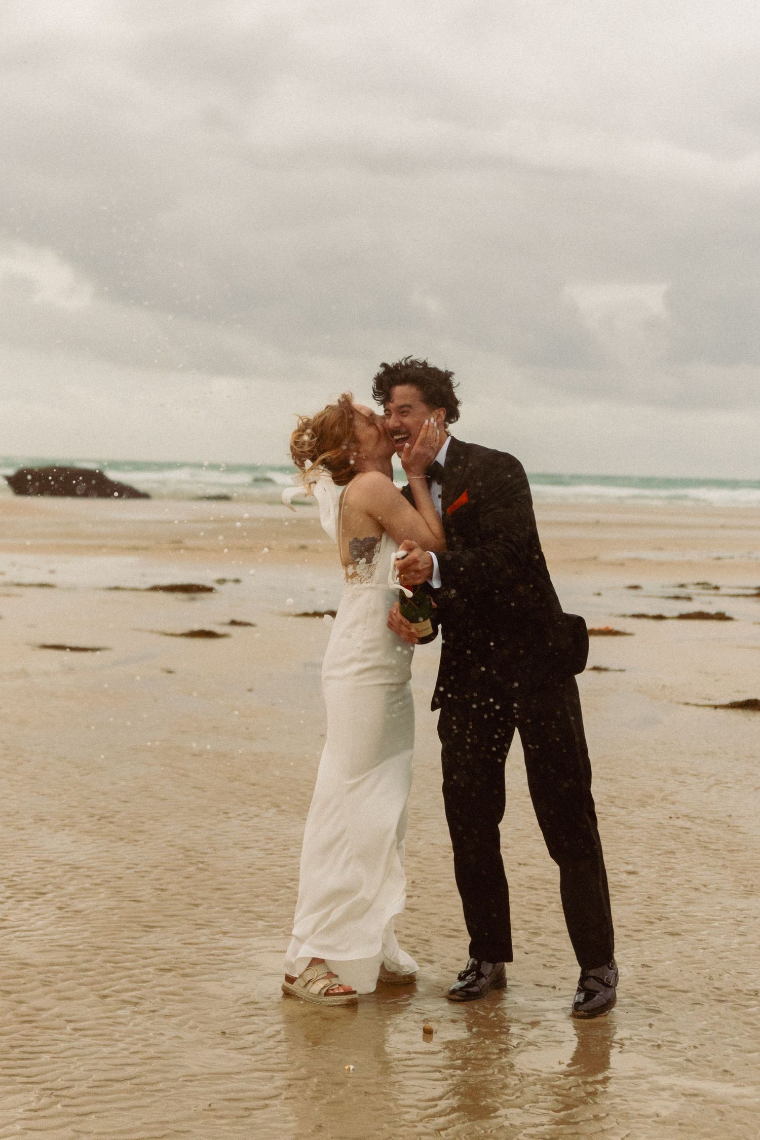 A bride in a short white dress and long veil holds a burgundy and blush bouquet in a misty countryside field.