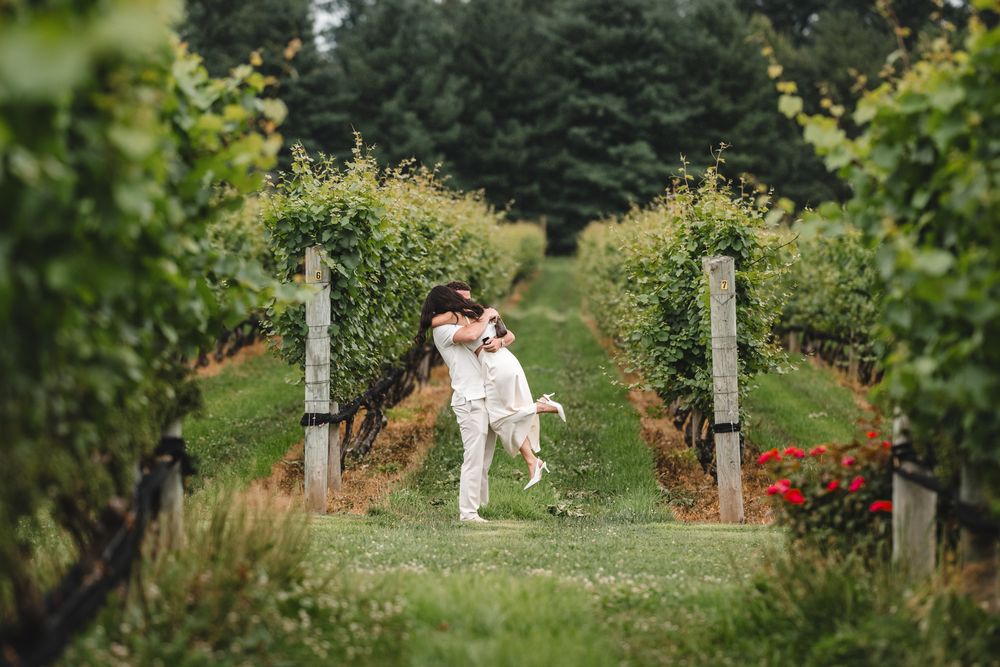 A joyful couple celebrating in a vineyard with one person being lifted in excitement.