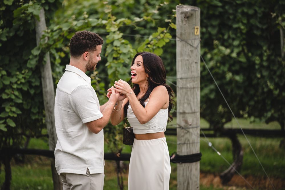 A couple reacting with excitement during a proposal in a lush vineyard setting.