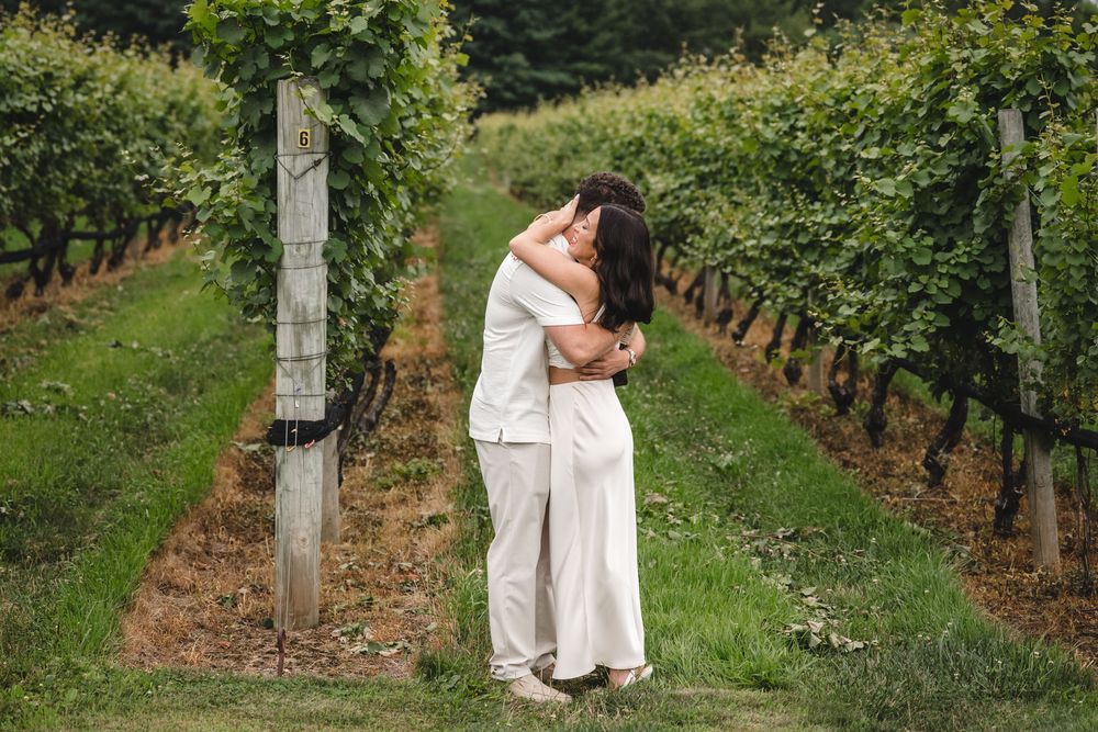 A couple sharing an intimate moment among the vineyard rows on a cloudy day.