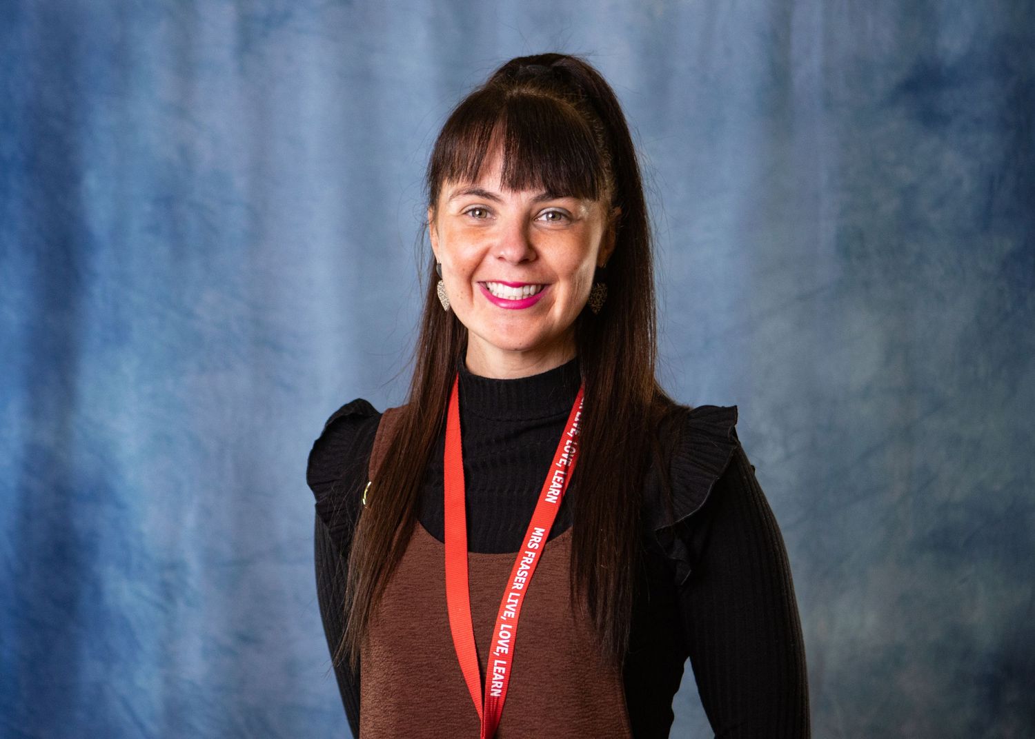 Professional headshot portrait against a blue background wearing a black turtleneck and bright smile.