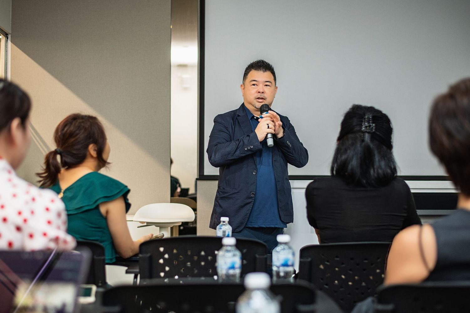 A group attends a business conference or meeting in a modern office setting with presentation screens visible.