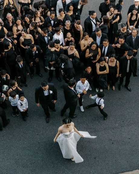 Someone wearing a black top holds up a white lace wedding dress on a hanger while looking at it excitedly.
