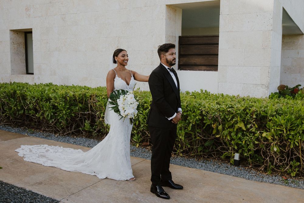 Bride and groom having their first look outside a modern white building with tropical landscaping.